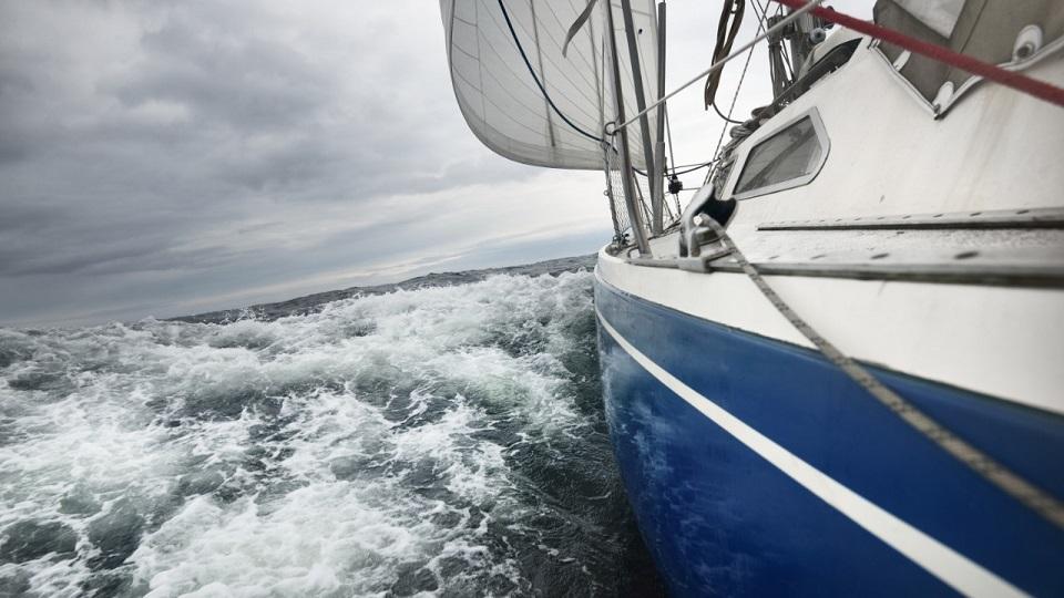 Yacht sailing during a thunderstorm on a rainy day. Close-up view from the deck to the bow, mast, sails. Dramatic sky. 